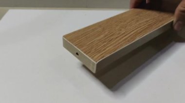 Bir adamın eli, beyaz bir tahtaya, açık kahverengi dikdörtgen tahta üzerine tek tek dizilmiş üç minimalist tahta yerleştirir. ahşap mobilyalar.