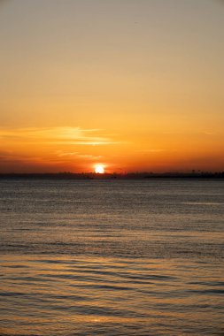 Sakin suların üzerinde sersemletici bir günbatımı Uzakta bir şehir silüeti