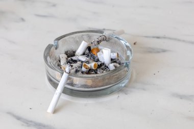 Kül tablası sigara izmaritleri ve küllerle dolu bir mermer yüzeyde.