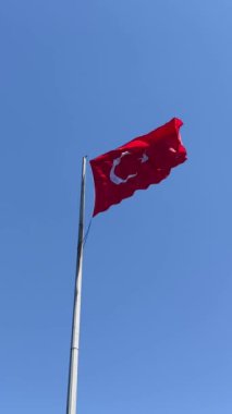 Turkish flag waves vibrantly in the wind on flagpole against clear blue sky