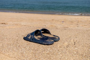 Yaz için parlak, kauçuk, yumuşak terlikler. Açık renkli köpükten yapılmış plaj terlikleri. Kumda bir çift terlik. Arka planda deniz doğal ışıkla çekiliyor.
