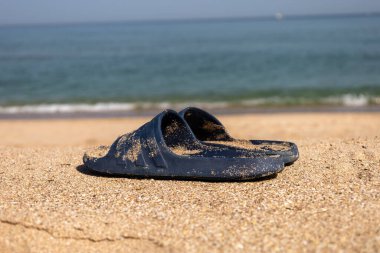 Yaz için parlak, kauçuk, yumuşak terlikler. Açık renkli köpükten yapılmış plaj terlikleri. Kumda bir çift terlik. Arka planda deniz doğal ışıkla çekiliyor.