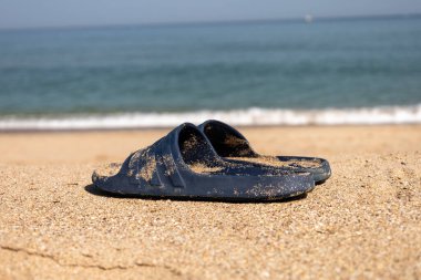 Yaz için parlak, kauçuk, yumuşak terlikler. Açık renkli köpükten yapılmış plaj terlikleri. Kumda bir çift terlik. Arka planda deniz doğal ışıkla çekiliyor.