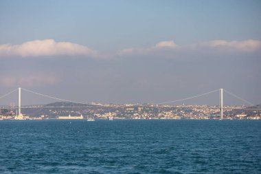 Bir boğaz köprüsü, arka planda bir şehir bulunan bir su kütlesi genişliğinde uzanır.