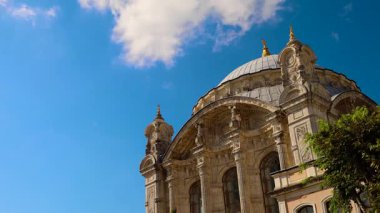 Tepesinde kubbe, arkasında mavi gökyüzü olan büyük bir bina. Ortak cami