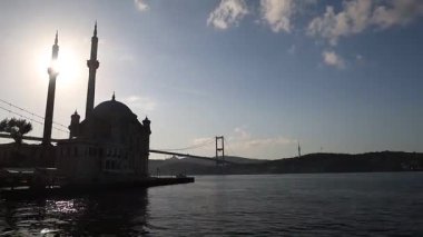 Büyük bir köprüsü ve büyük bir camisi olan güzel bir şehir. Gökyüzü açık ve güneş parlıyor.