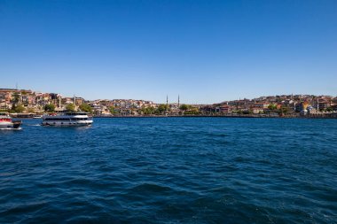 Sudaki tekneler, açık gökyüzü altındaki camilerle şehir silueti..