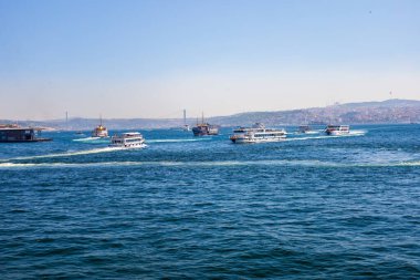 Mavi denizde feribot, şehir silueti ve uzak köprü..