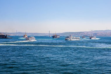 Mavi denizde feribot, şehir silueti ve uzak köprü..