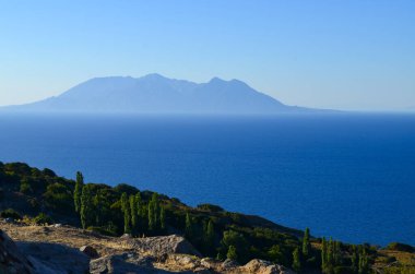 Arkasında dağ olan güzel mavi bir okyanus. Gökyüzü açık ve güneş parlıyor.