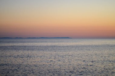 Okyanus sakin ve gökyüzü güzel turuncu bir renktir. Güneş batıyor, sıcak ve huzurlu bir atmosfer yaratıyor.