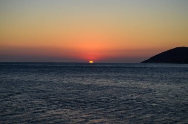Okyanus sakin ve gökyüzü güzel turuncu bir renktir. Güneş batıyor, sıcak ve huzurlu bir atmosfer yaratıyor.