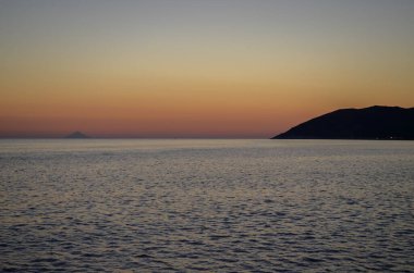 Okyanus sakin ve gökyüzü güzel turuncu bir renktir. Güneş batıyor, sıcak ve huzurlu bir atmosfer yaratıyor.