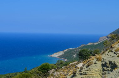 Arkasında dağ olan güzel mavi bir okyanus. Gökyüzü açık ve güneş parlıyor.