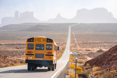Monument Valley, ABD. 16 Eylül 2022. Okul otobüsü Anıt Vadisi 'ne doğru ilerliyor. Toplu taşıma, çöl manzarası arasında hareket ediyor. Yaz boyunca jeolojik özelliklerin görünümü.