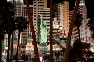 Las Vegas, ABD. 16 Eylül 2022. New York, New York, New York Otel ve Kumarhanesi 'ndeki Özgürlük Anıtı ve hız treninin kopyası. Las Vegas 'ta gece ağaçların arasından görünen aydınlık binalar..