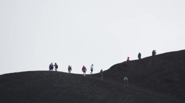 Volkanik Etna Dağı 'nda yürüyüş yapan turistler. İnsanlar ünlü bir yerde maceralı tatilin tadını çıkarıyorlar. Arka planda dumanla kaplı gökyüzü ile dramatik manzara. Etna Dağı tırmanılıyor.