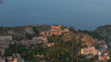 Sicilya, Taormina 'daki Antik Yunan Tiyatrosu' nun kalıntılarının havadan görünüşü İyon Denizi 'nin Giardini-Naxos körfezine sabah güneşi altında uzanan Etna' nın dumanlı kuyruğuyla yayılıyor..