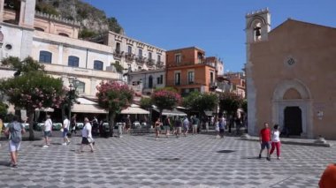 Erkek ve kadın turistler güneşli bir günde eski kasaba meydanını keşfediyorlar. Antik çan kulesi ve kıyı şehrindeki tarihi binalar..