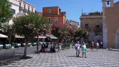 Erkek ve kadın turistler güneşli bir günde eski kasaba meydanını keşfediyorlar. Antik çan kulesi ve kıyı şehrindeki tarihi binalar..