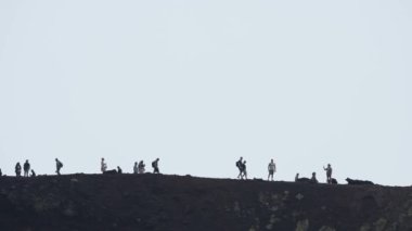 Volkanik Etna Dağı 'nda yürüyüş yapan turistler. İnsanlar ünlü bir yerde maceralı tatilin tadını çıkarıyorlar. Arka planda dumanla kaplı gökyüzü ile dramatik manzara. Etna Dağı tırmanılıyor.