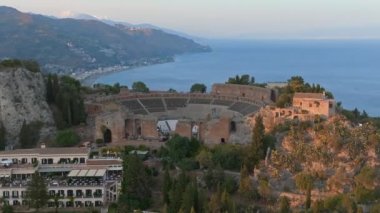 Sicilya, Taormina 'daki Antik Yunan Tiyatrosu' nun kalıntılarının havadan görünüşü İyon Denizi 'nin Giardini-Naxos körfezine sabah güneşi altında uzanan Etna' nın dumanlı kuyruğuyla yayılıyor..