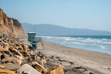 Kumlu kumsaldaki cankurtaran kulesi ve güneşli bir günde San Diego 'nun arka planında berrak mavi gökyüzü ile denize vuran dalgaların manzarası.