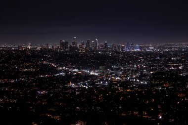 Los Angeles 'ın modern şehir merkezindeki aydınlık binaların ve gökdelenlerin hava manzarası ve gece vakti karanlık gökyüzü.