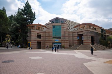 Los Angeles, ABD. 20 Eylül 2022. UCLA binasının arka planında bulutlu gökyüzü olan kampüste ve dışında yürüyen öğrenciler.