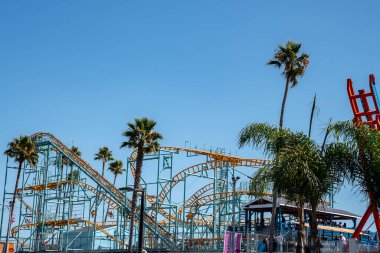 Santa Cruz, ABD. 20 Eylül 2022. Güneşli bir günde Santa Cruz Sahilinin arka planında açık mavi gökyüzü olan renkli lunapark trenlerinin ve palmiye ağaçlarının alçak açılı görüntüsü