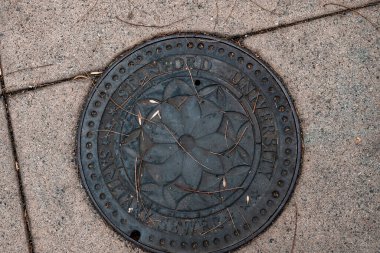 Stanford Üniversitesi ve Palo Alto 'daki kampüste yaya yolunu kaplayan hijyenik kanalizasyon yazısıyla birlikte yüksek açılı siyah metalik rögar deliği.