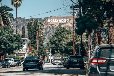Los Angeles, ABD. 20 Eylül 2022. Ağaçların arasında yol alan arabalar güzel Lee Dağı 'na doğru ilerliyorlar. Güneşli bir günde, arka planda açık gökyüzü olan Hollywood tabelasıyla.