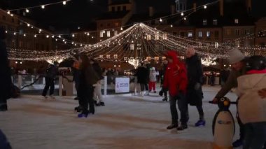 Mutlu insanlar Polonya 'nın eski Varşova kasabasının ortasında buz pateni yapıyorlar. Noel pazarının güzel Noel süsleme ışıkları.