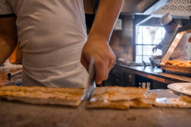 Erkek şefin orta bölümü restoranda ticari mutfakta Türk peynirini dilimlere ayırıyor.