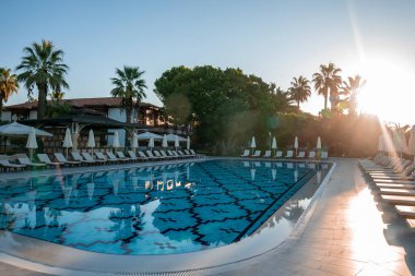 Boş şezlonglar ve güneşli bir günde turistik bir otelde yüzme havuzunun etrafına yerleştirilmiş katlanmış şemsiyeler.