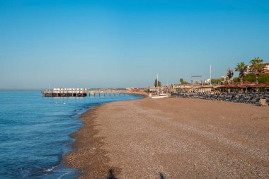 Deniz manzarası ve kumlu sahil manzarası. Boş güverte sandalyeleri ve güneşli bir günde açık mavi gökyüzü olan şemsiyeler.