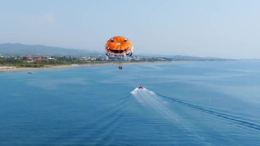Paraşütle atlama sahnesi. Aktif bir eğlence şekli. Hareketli bir tekneye uzun bir iple bağlanan bir insan ve havada süzülen özel paraşüt sayesinde.