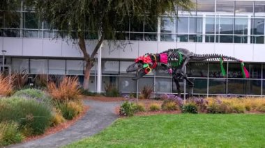 Statue of dinosaur skeleton decorated with colorful fabrics and artificial flowers by plants in campus of Google office