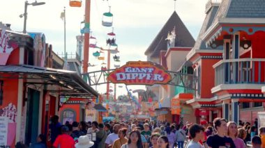 Beautiful summer day in Santa Cruz. People enjoying amusement park at Santa Cruz and Beach Boardwalk with clear blue sky in the background.