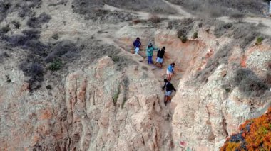 Group of people climbing down the cliff to get to the beach by the Pacific ocean.