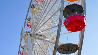 Ferris wheel and roller coaster rides and people exploring shops at the Pacific amusement park on the Santa Monica Pier.