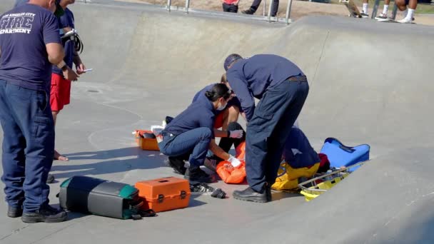 消防士とライフガードはスケートボードパークのランプで負傷者を調べ 人々は晴れた日にヴェネツィアのビーチスケートパークで手すりによって — ストック動画