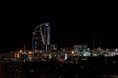 Distant view of illuminated W letter on top of luxurious W Barcelona Hotel and buildings under sky at night in Barcelona, Spain