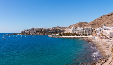 Aerial view of beach and ships sailing on beautiful seascape by buildings at coastline with clear blue sky in the background. A sunny day at Gran Canaria island in Spain