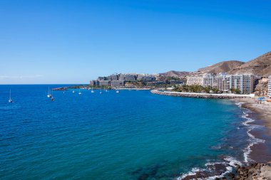 İspanya, Gran Canaria 'daki sahil şeridi boyunca inşa ve dağ ile güzel mavi deniz manzarasında seyreden gemiler.