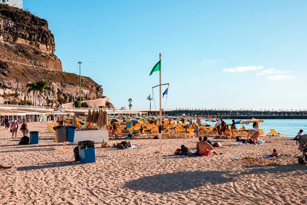 スペイン グラン カナリアの明るい夏の日に青い空と岩の崖と砂浜のリゾートで日光浴をする観光客 — ストック写真