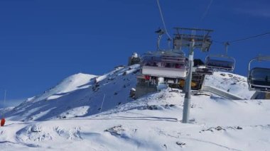Zirve manzaralı kayak koltuğu kaldırma ve yamaçlar. Mavi gökyüzü ve parlak güneşle kar üstüne güzel bir kayak merkezi. Kayak kulübeleri, kayakçılar ve snowboardcular.. 