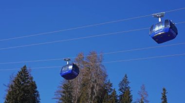 Zirve manzaralı kayak koltuğu kaldırma ve yamaçlar. Mavi gökyüzü ve parlak güneşle kar üstüne güzel bir kayak merkezi. Kayak kulübeleri, kayakçılar ve snowboardcular.. 