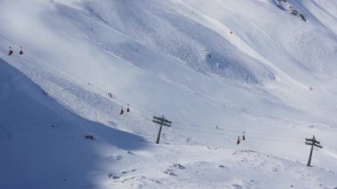 Zirve manzaralı kayak koltuğu kaldırma ve yamaçlar. Mavi gökyüzü ve parlak güneşle kar üstüne güzel bir kayak merkezi. Kayak kulübeleri, kayakçılar ve snowboardcular.. 