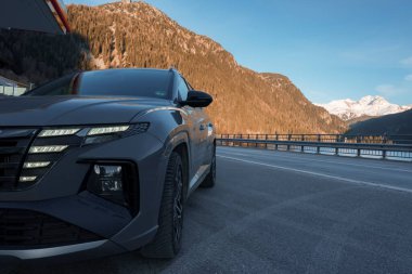 Yepyeni Hyndai Tucson 2023 SUV aracı yolun kenarına park edilmiş ve arka planda İsviçre 'de dağ aralığı ve berrak bir gökyüzü var..